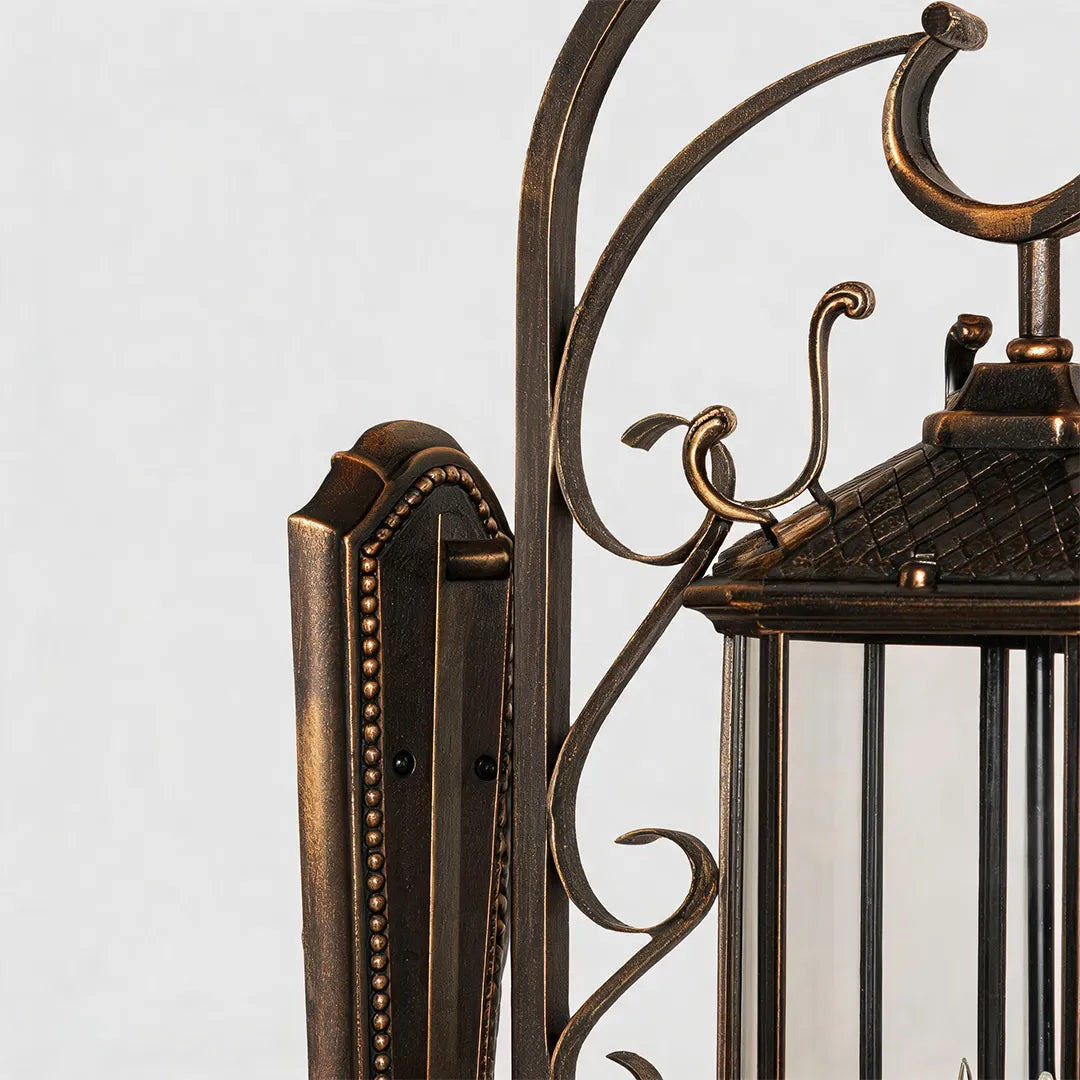 Black outdoor lantern sconce detail showing the decorative scroll arm, textured backplate, and traditional metal craftsmanship.