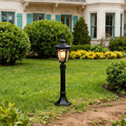 A classic black outdoor light post standing on green grass in front of a white house with blue.