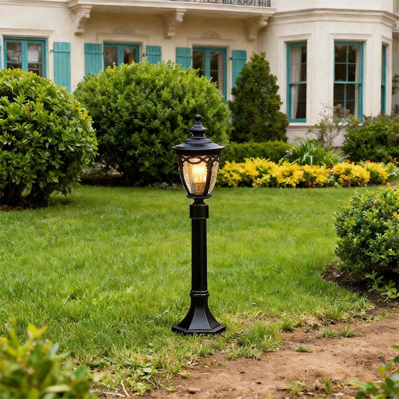 A classic black outdoor light post standing on green grass in front of a white house with blue.