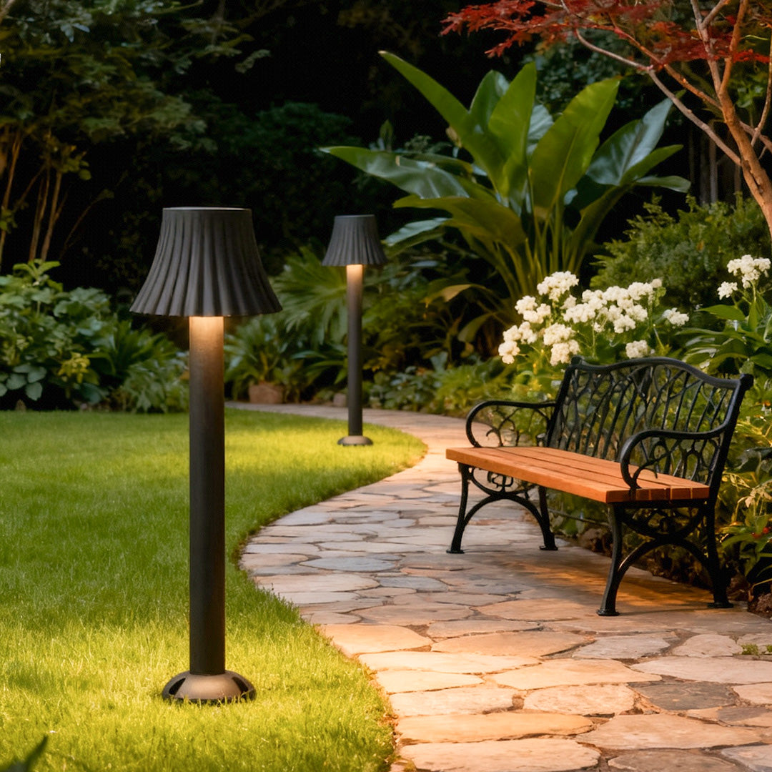 Black outdoor path light standing along a garden pathway surrounded by lush greenery.