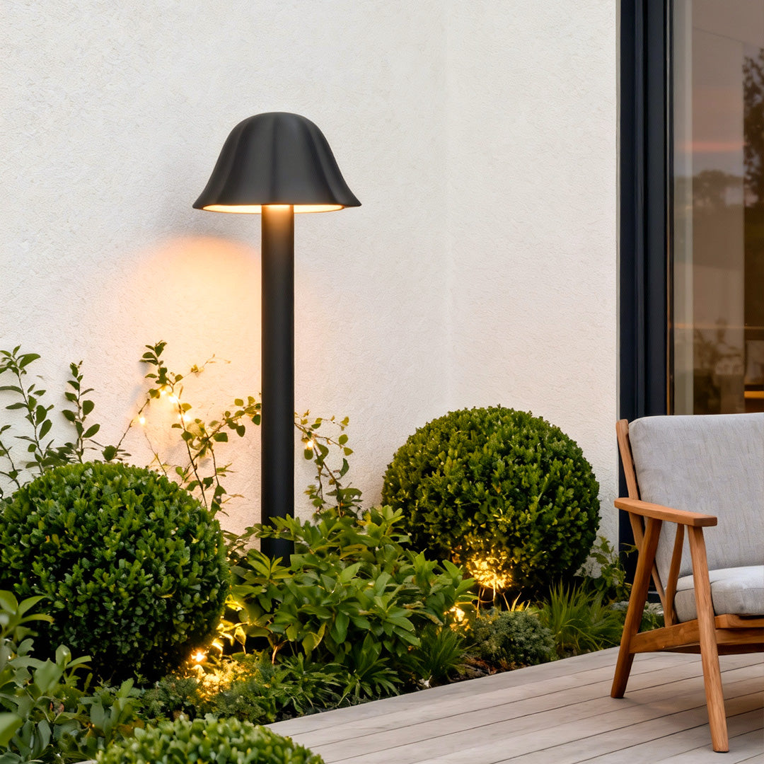 Black outdoor path light placed near shrubs and a minimalist outdoor seating area.