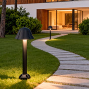 Black outdoor path light lighting up a soft-curve pathway leading to a modern house entrance.