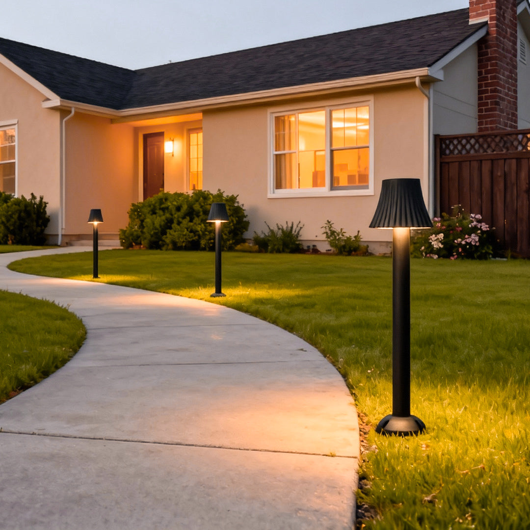 Warm-lit black outdoor path light illuminating a curved walkway beside a modern home façade.