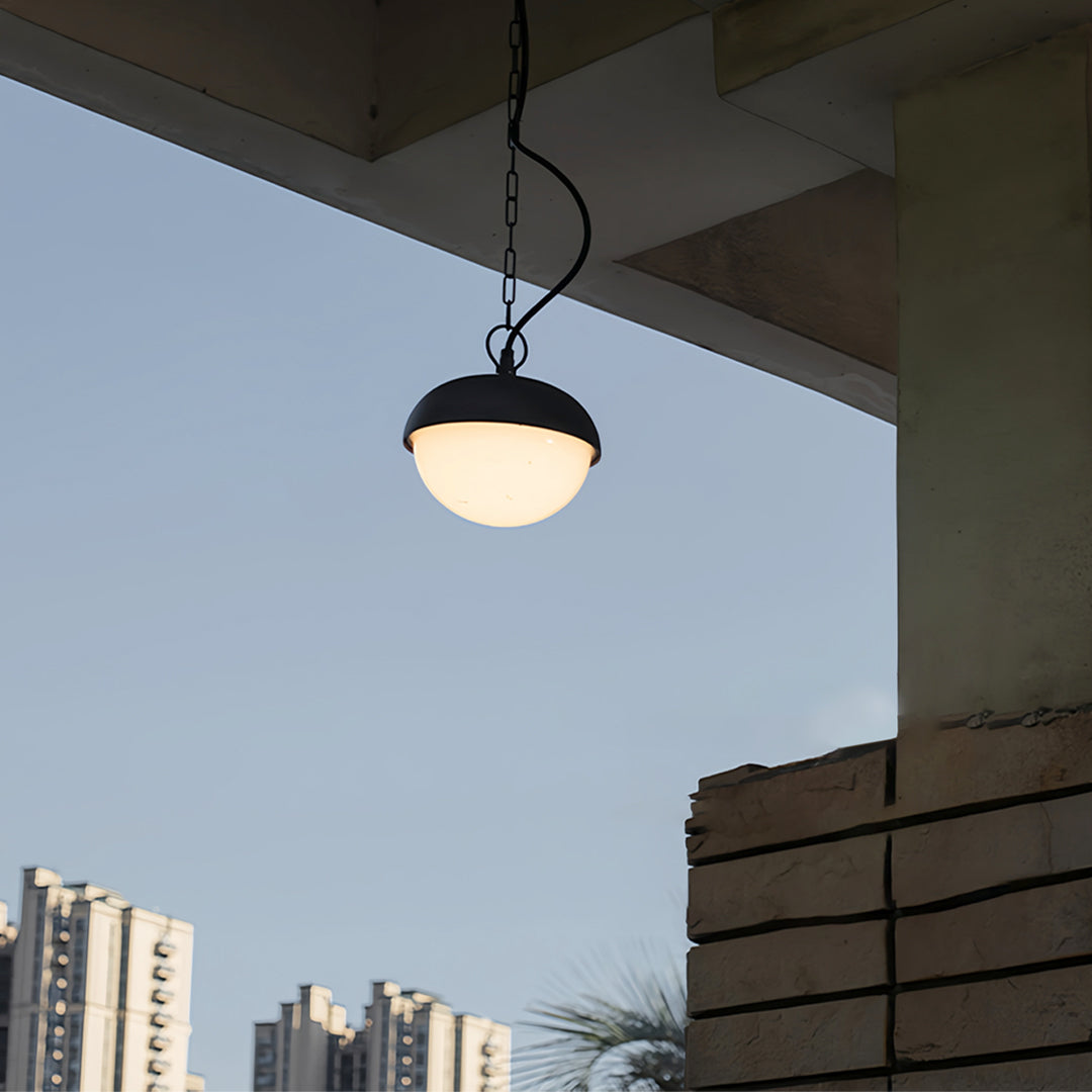 Black outdoor pendant light hanging on a balcony ceiling with city skyline visible in the background.