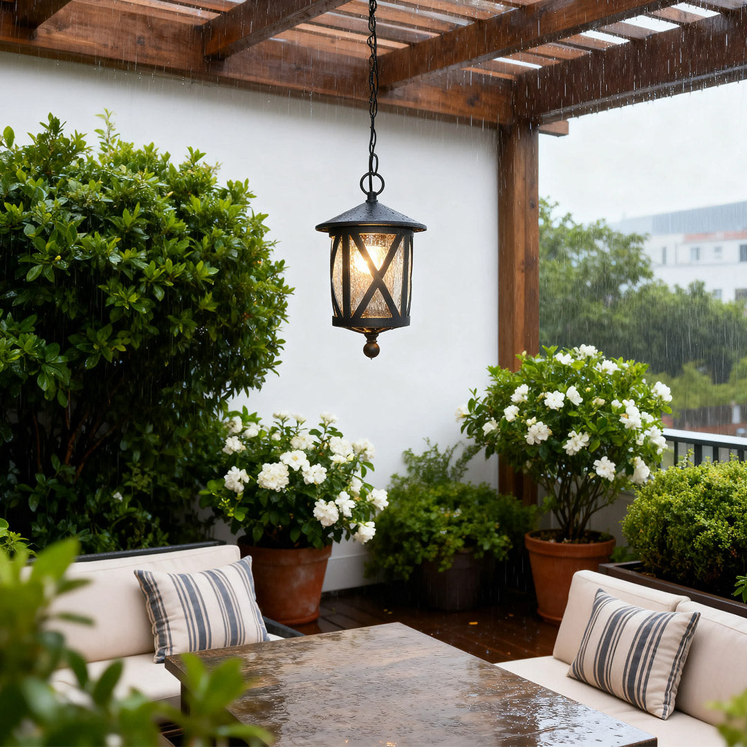 Black outdoor pendant light suspended from covered patio with white columns and lush greenery view