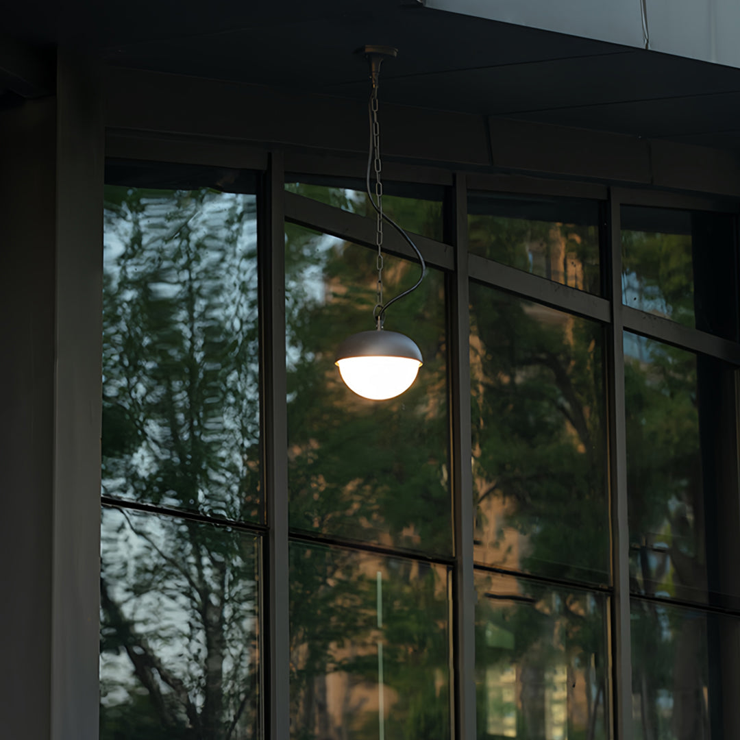 Elegant black outdoor pendant light hanging near large windows, providing warm illumination during dusk.