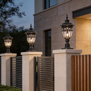 Classic black outdoor pillar light with intricate metalwork, installed on a stone pillar near a modern house.