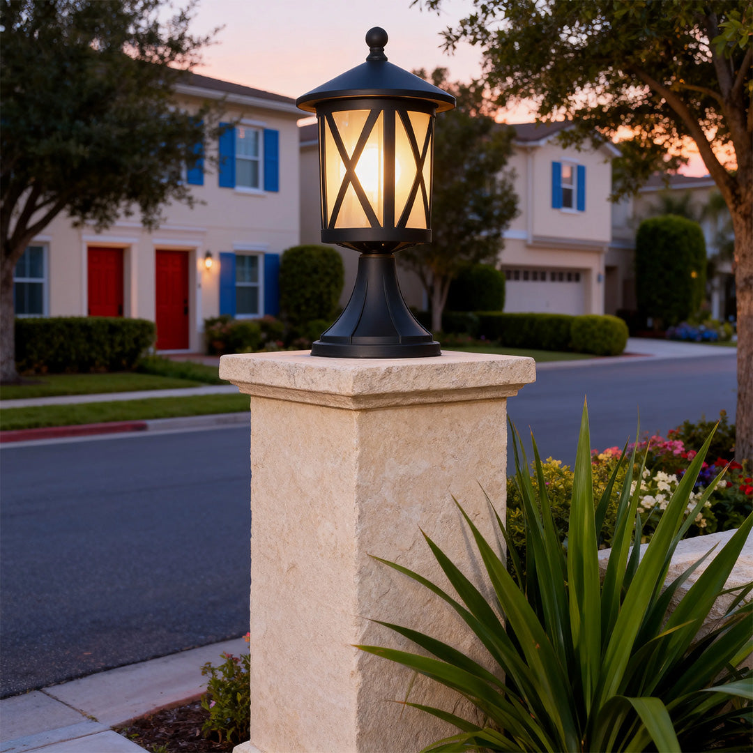 Black outdoor pillar light providing warm illumination on beige column at residential street corner during twilight