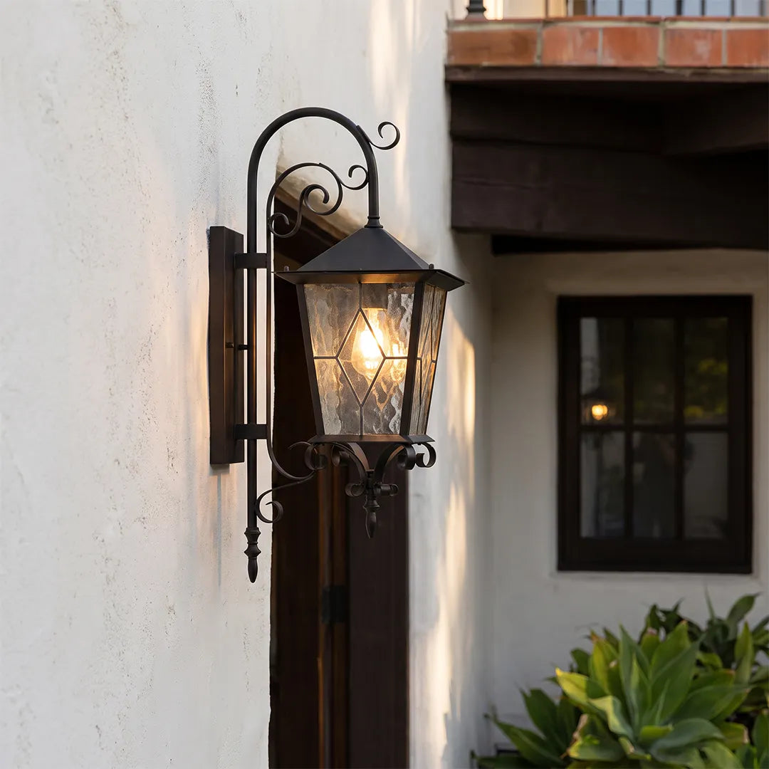 Black outdoor sconce mounted on a white exterior wall, featuring a hanging lantern design with decorative scroll arm.