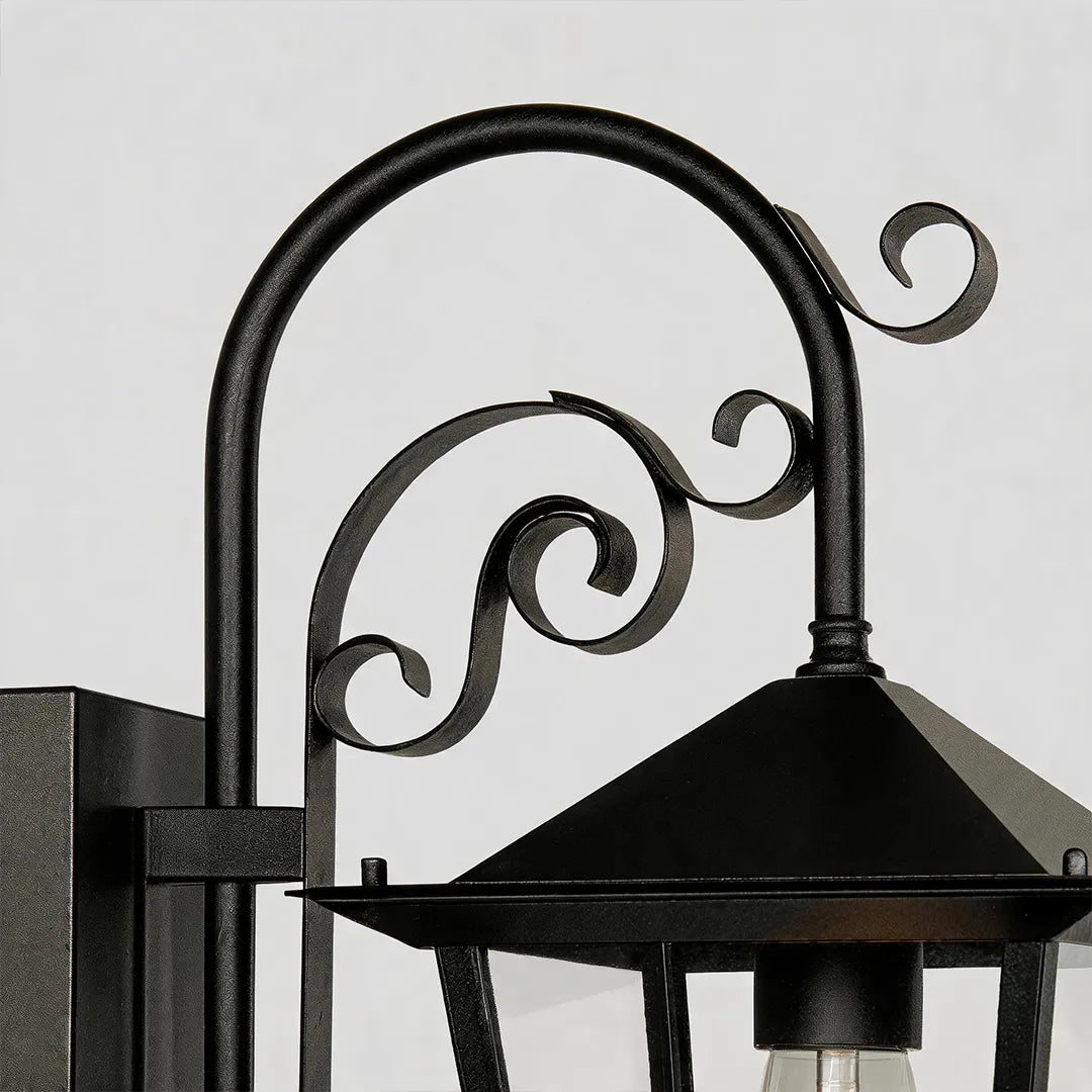 Black outdoor sconce detail highlighting the curved scroll arm and decorative metal mounting design.
