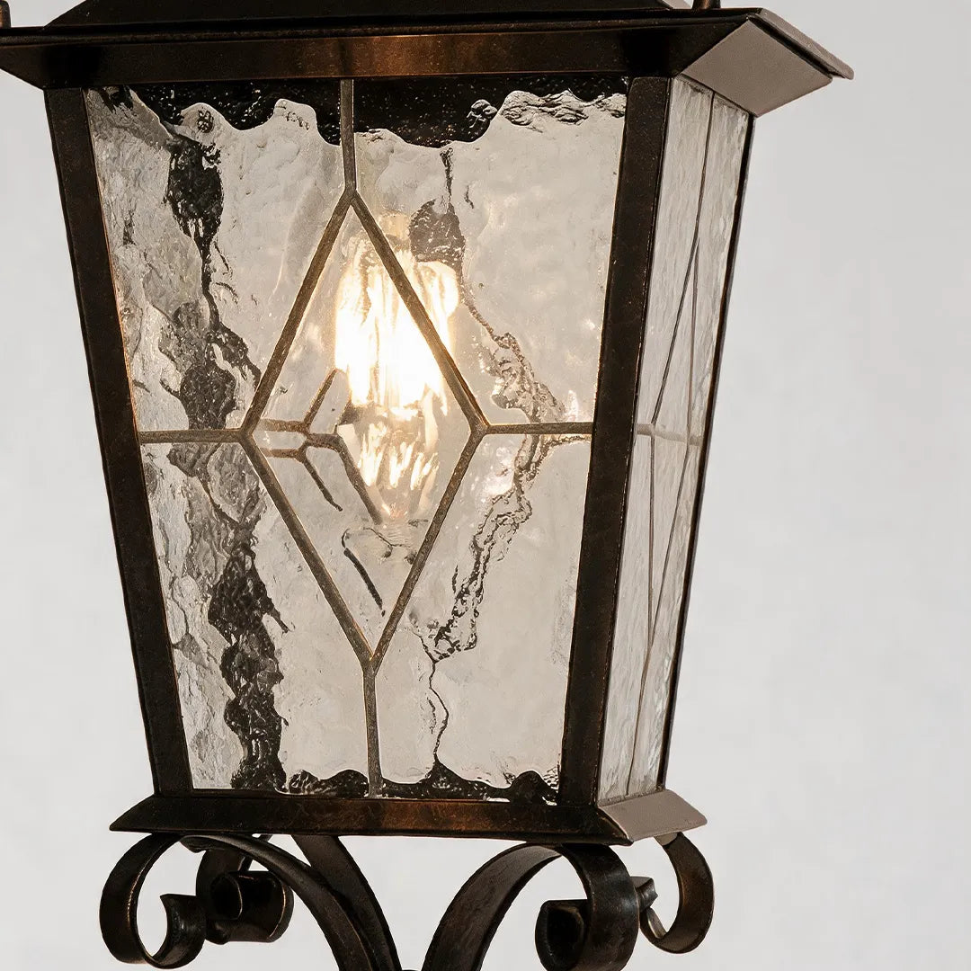 Black outdoor sconce close-up showing seeded glass panels, metal lantern frame, and exposed bulb detail.