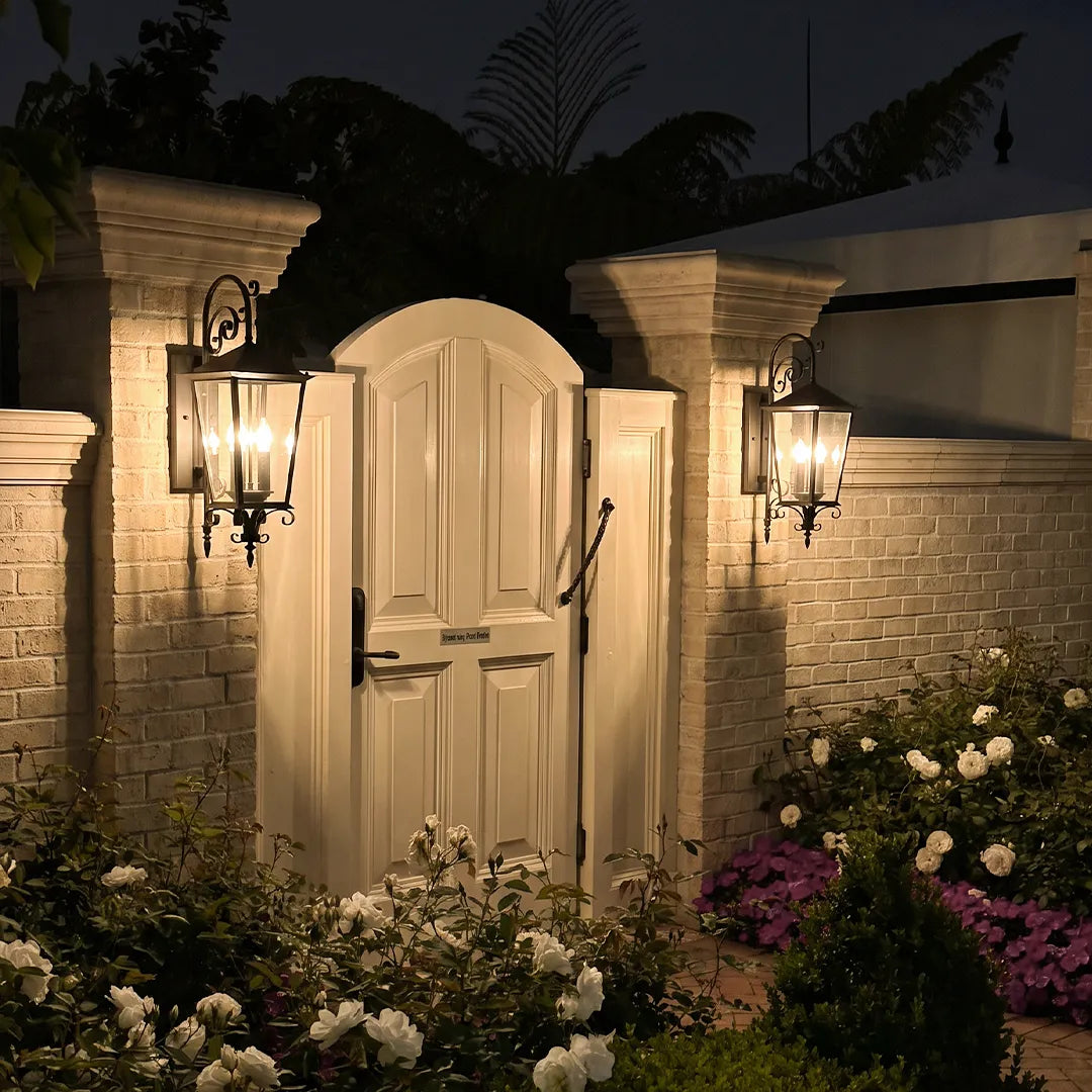 Black outdoor sconces installed around a garden gate, enhancing the entry with classic lantern-style wall lighting.