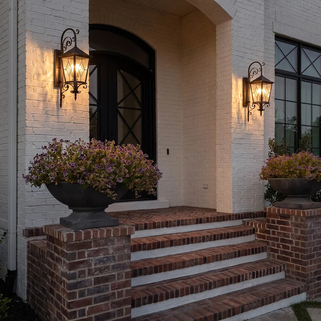 Black outdoor sconces flanking a brick front staircase, bringing warm traditional lighting to the home entrance.
