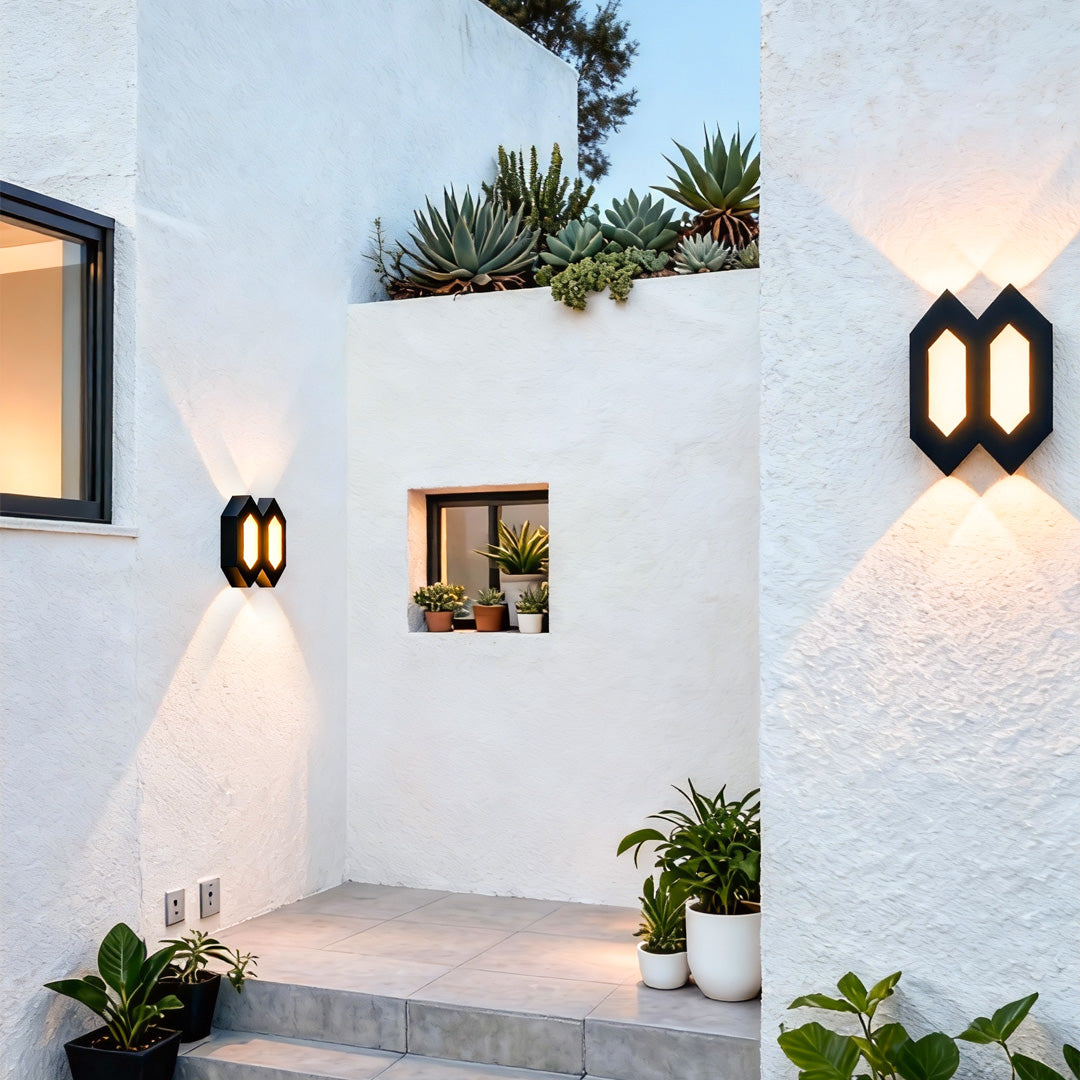 Geometric black outdoor up and down wall lights mounted on a bright white exterior wall, enhancing a landscaped walkway.