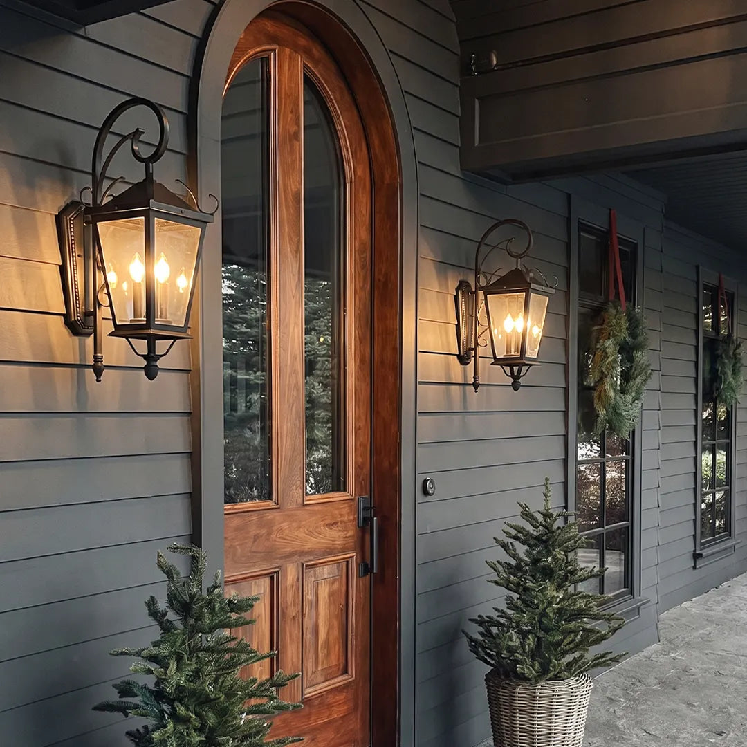 Black outdoor wall light mounted beside a tall arched wood front door, bringing classic lantern-style illumination to the entryway.
