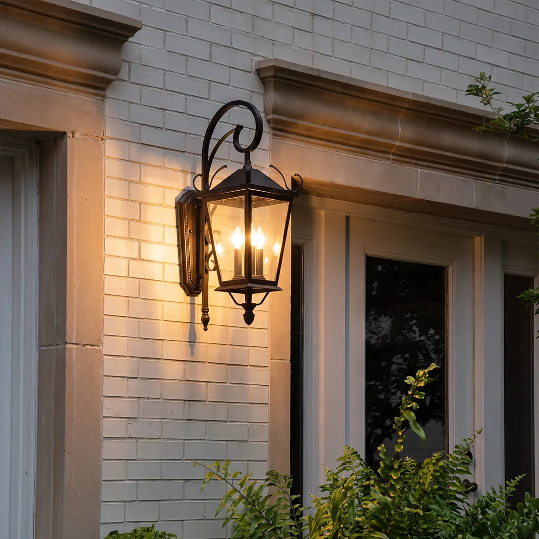 Black outdoor wall light fixed beside a front entry, providing warm lantern-style lighting for the exterior facade.