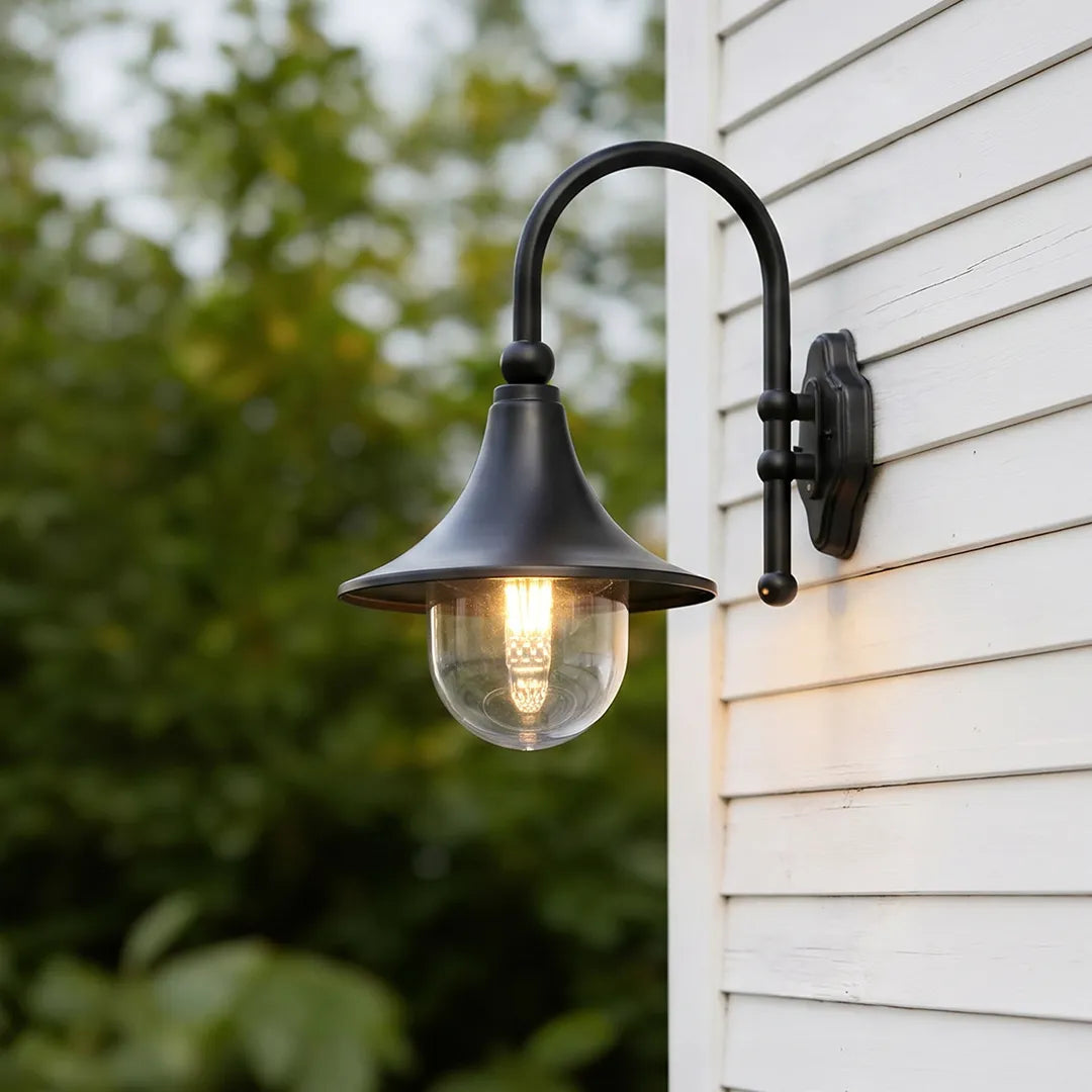 Black outdoor wall light with a curved arm and clear globe shade mounted on white exterior siding.