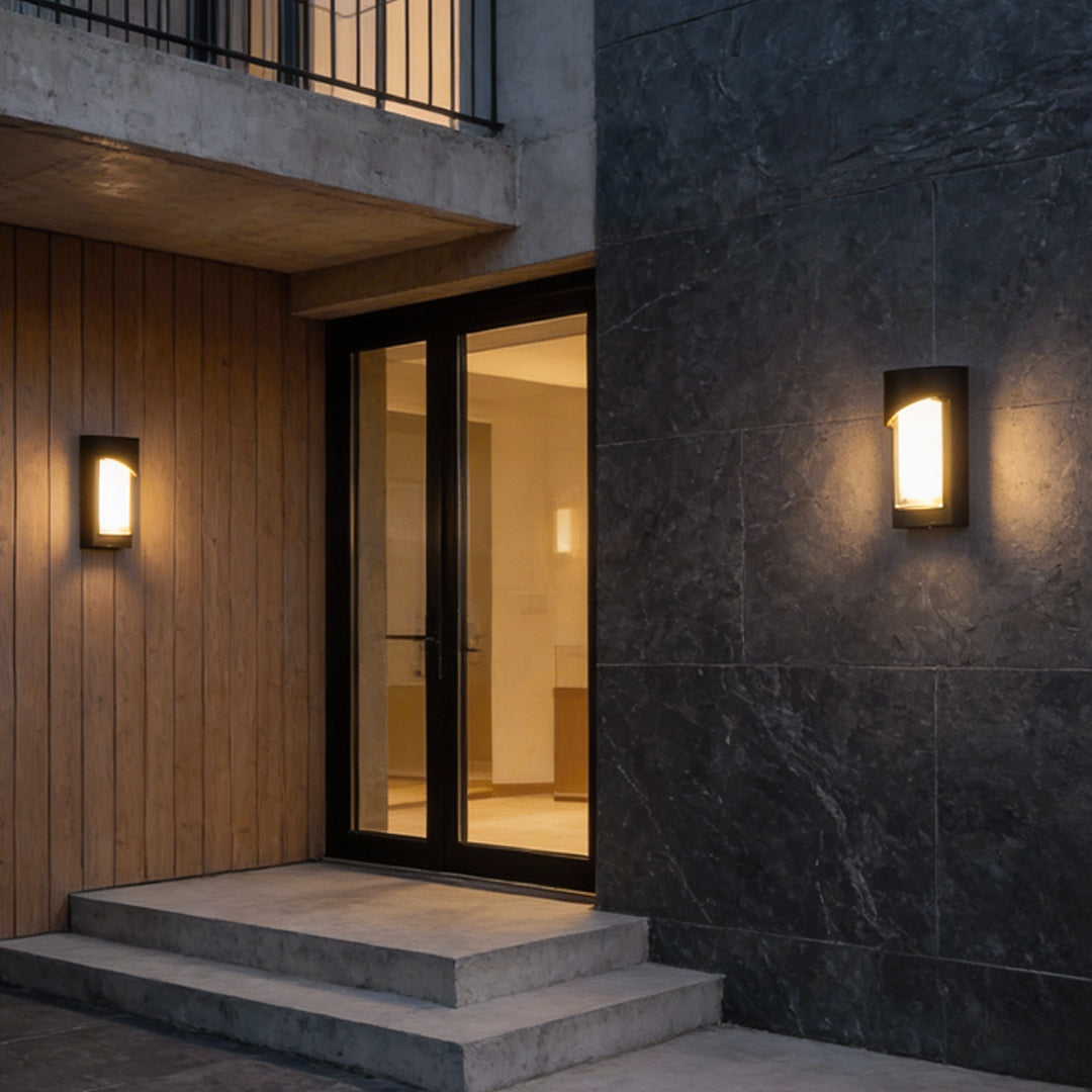 Black outdoor wall light illuminating entrance steps of modern house with warm glow.