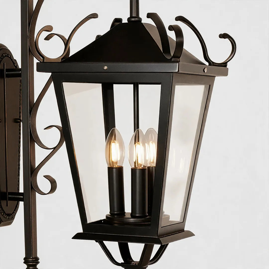 Black outdoor wall light close-up showing the lantern frame, candle-style bulbs, and ornate scroll accents.