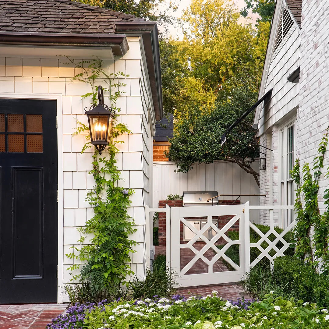 Black outdoor wall light mounted on white siding near a porch gate, adding decorative lantern-style lighting to the walkway.