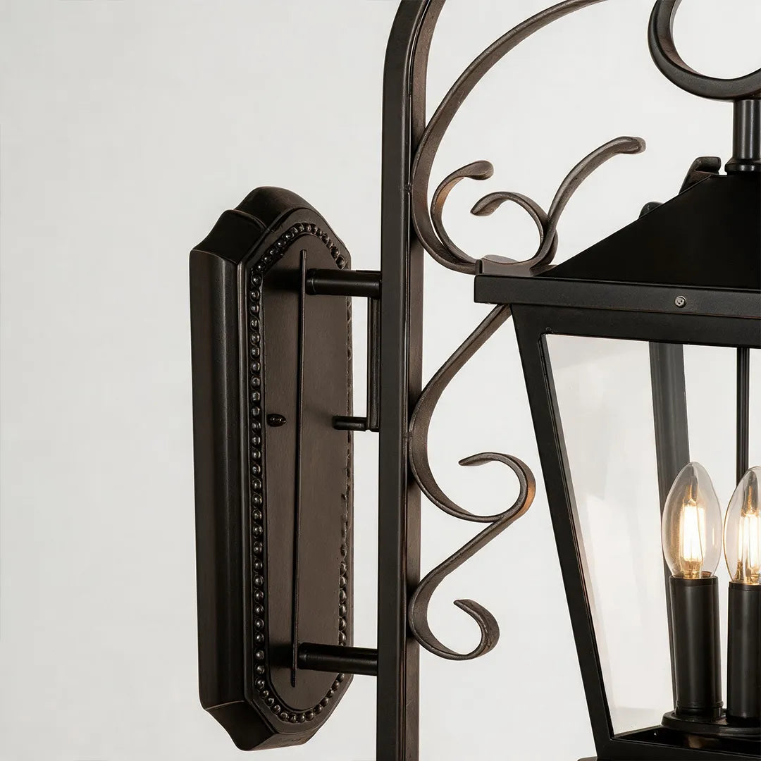 Black outdoor wall light detail view showing the side profile, mounting plate, and decorative scrollwork of the lantern fixture.