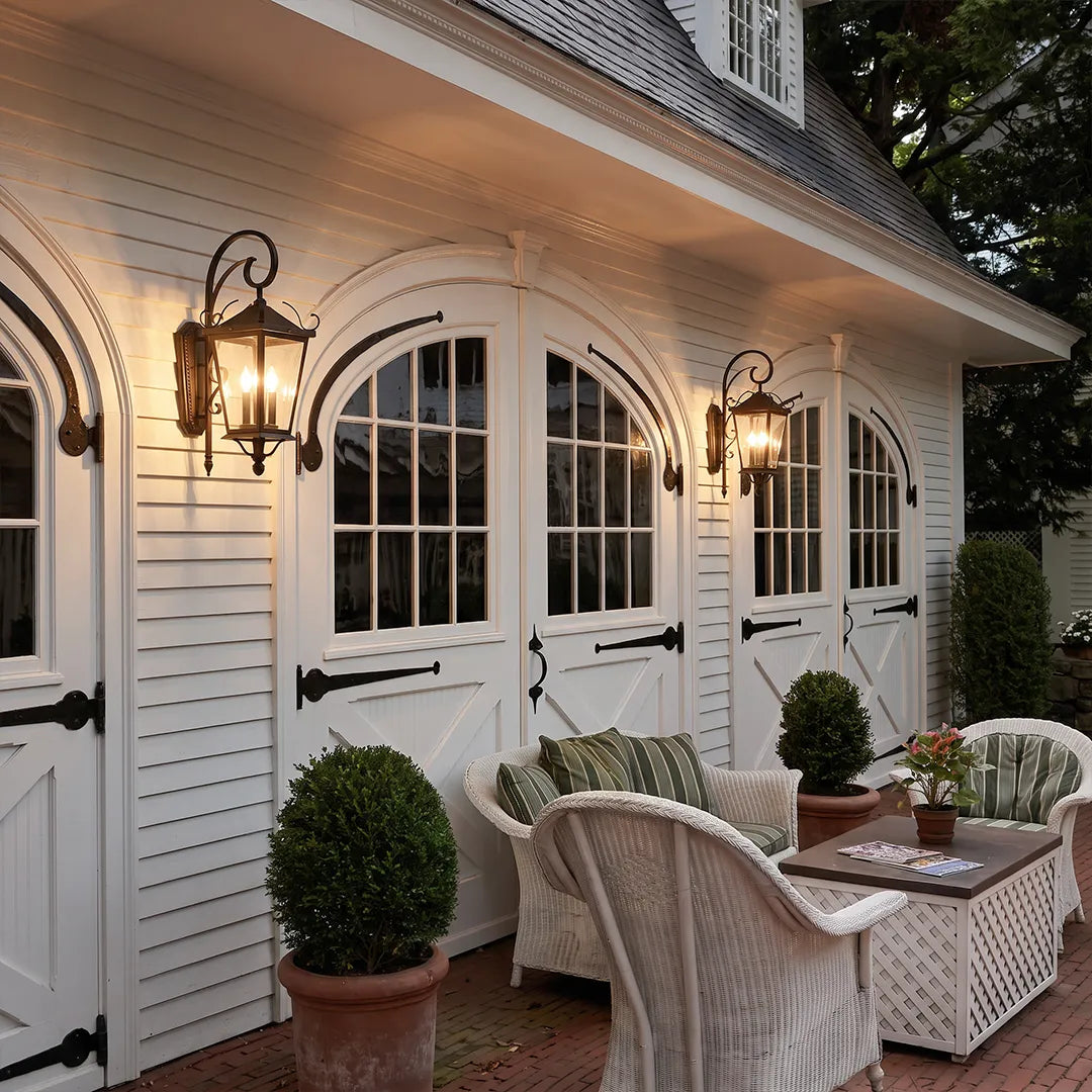 Black outdoor wall lights installed above white garage doors, adding traditional lantern-style lighting to the exterior seating area.