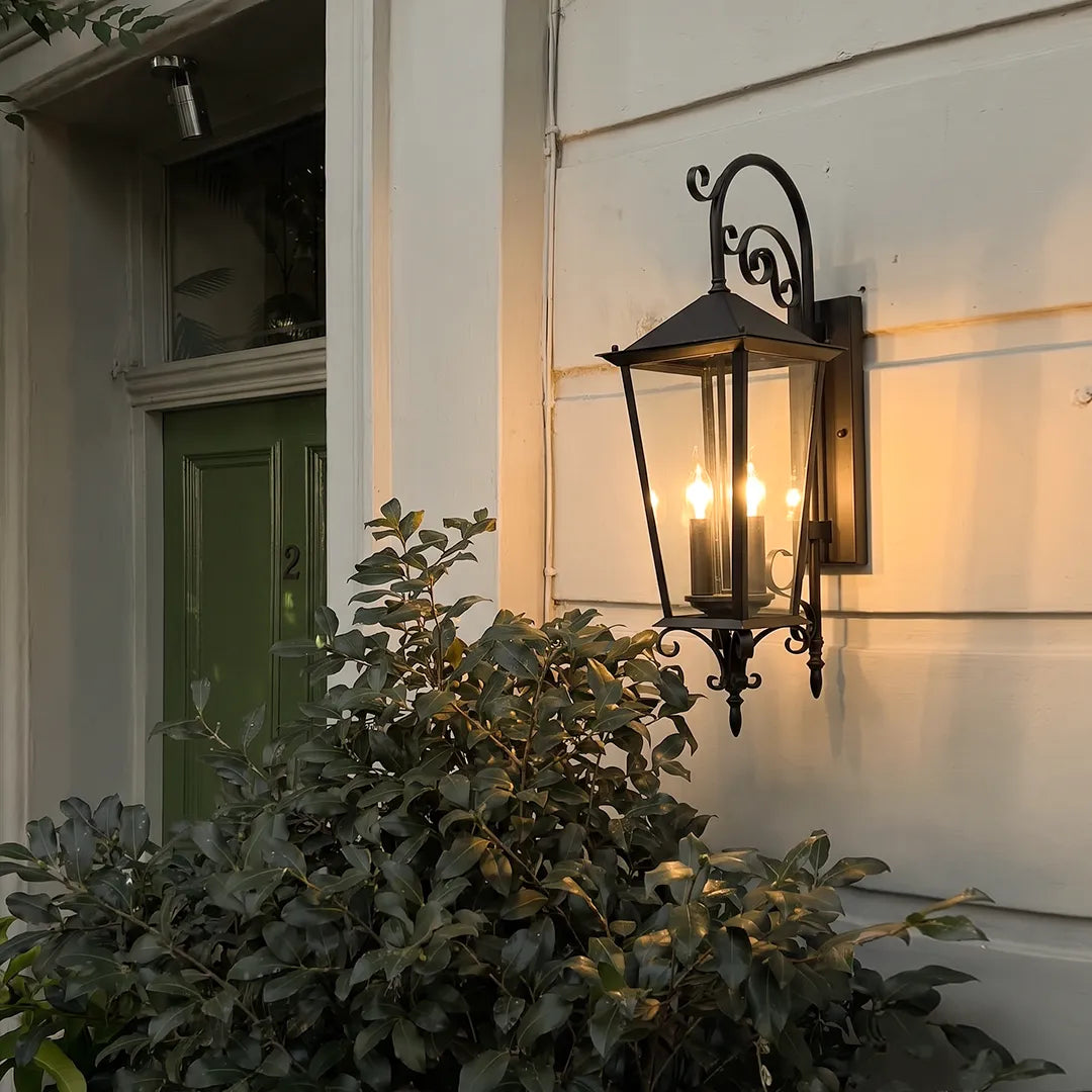 Black outdoor wall sconce mounted beside a green front door, bringing classic lantern-style accent lighting to the entryway.