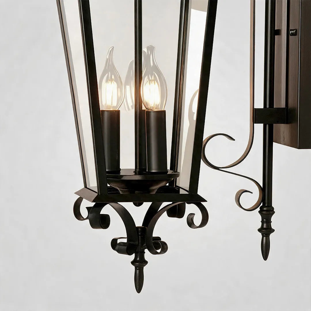 Black outdoor wall sconce detail view highlighting the lantern frame, candle-style bulbs, and decorative bottom finial.