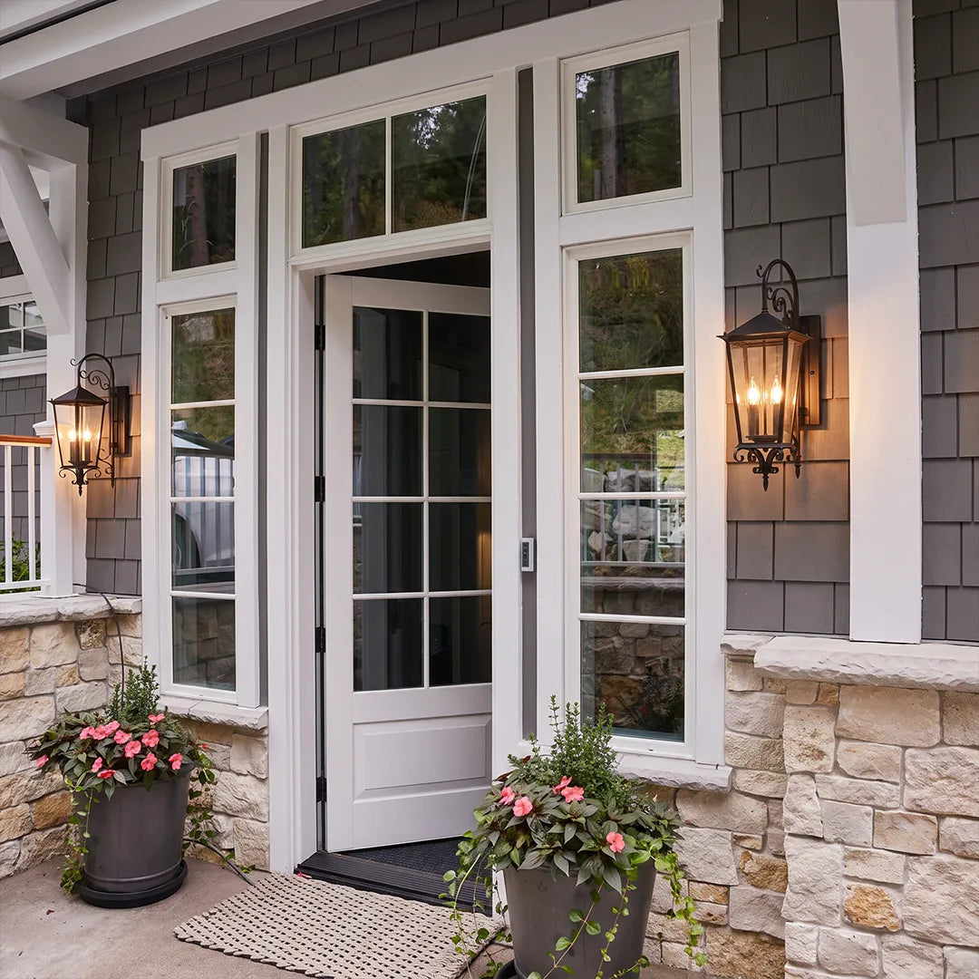 Black outdoor wall sconce installed next to a white patio door, adding warm lantern-style lighting to the stone and siding exterior.