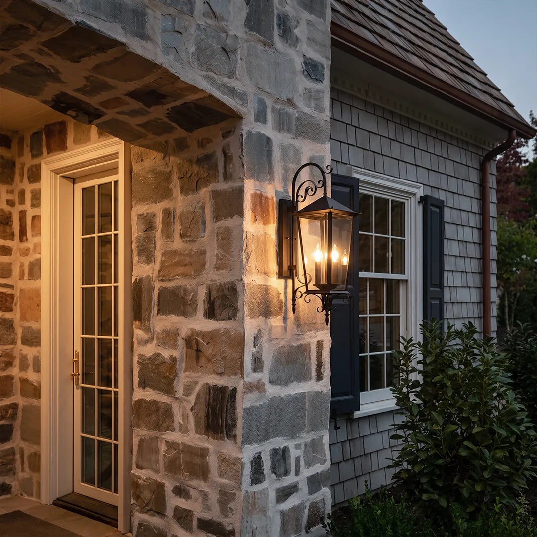 Black outdoor wall sconce installed on a stone exterior wall near a front entry, creating a warm welcoming glow