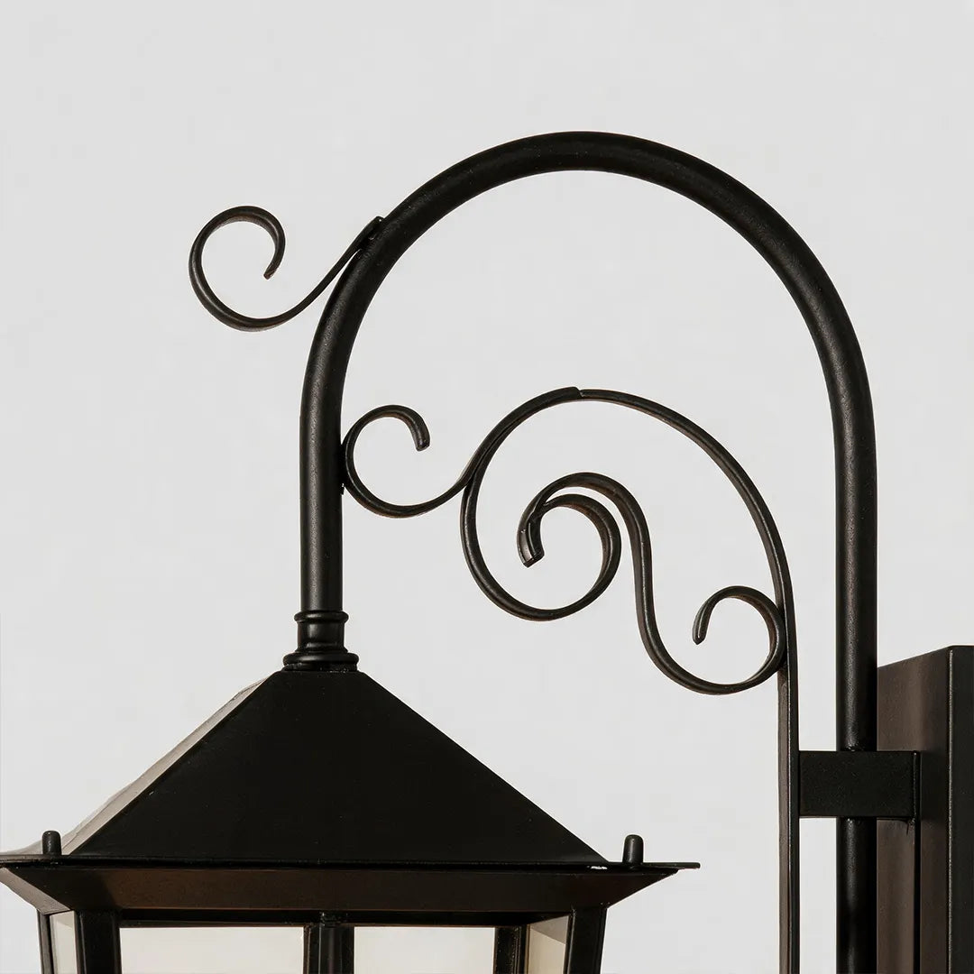 Black outdoor wall sconce close-up showing the curved scroll arm and top cap of the lantern fixture.