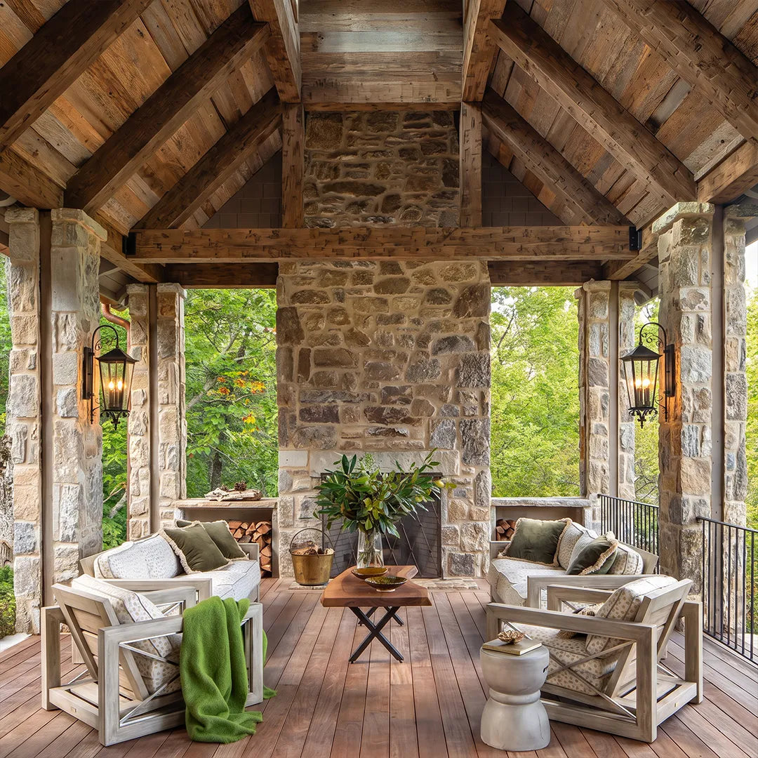 Black outdoor wall sconces illuminating a rustic covered porch with stone columns and wood ceiling beams.