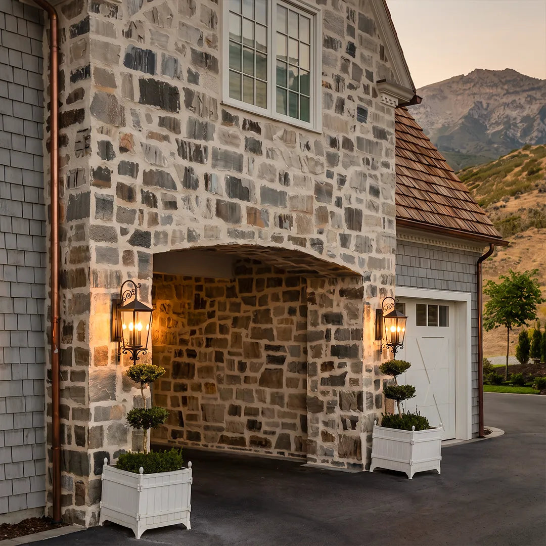 Black outdoor wall sconces flanking a stone garage entrance, providing traditional exterior lighting for the home facade.