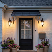 Black outside wall lights flanking a dark front door beneath a metal awning on a brick home.