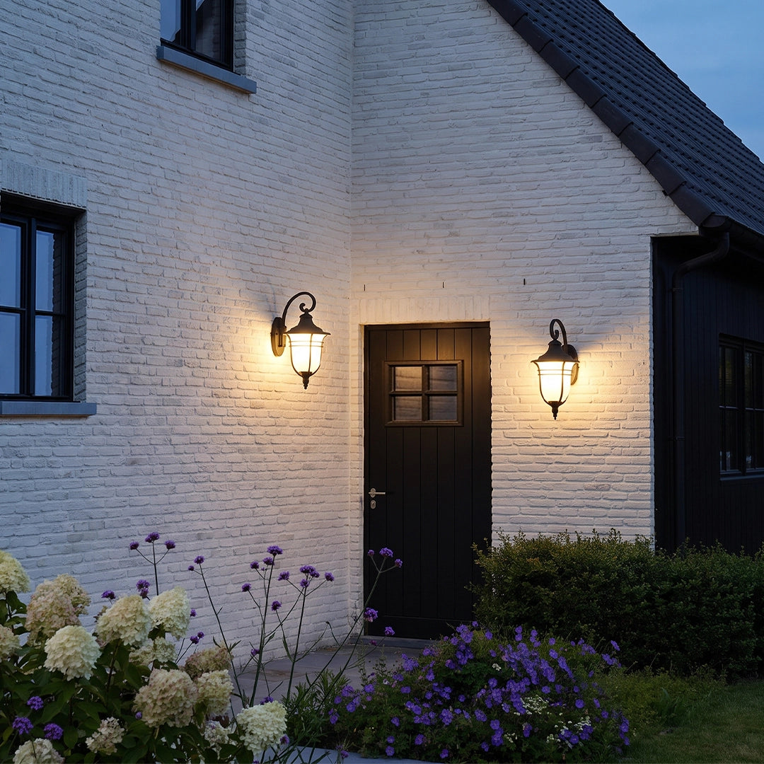 Black outside wall lights illuminating a side entrance surrounded by garden flowers and white brick.