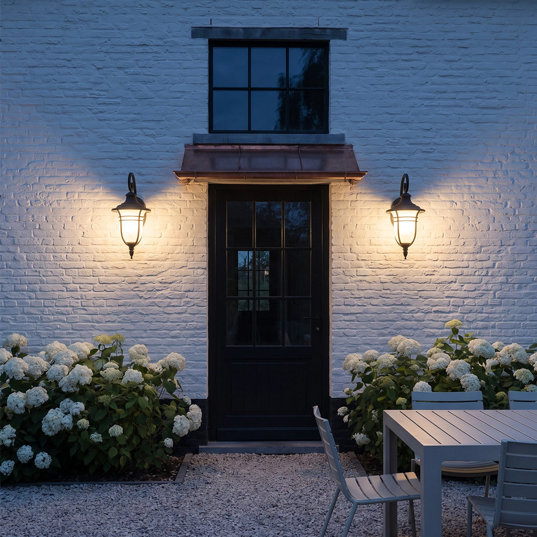 Black outside wall lights mounted beside a glass entry door with warm light across a white brick wall.