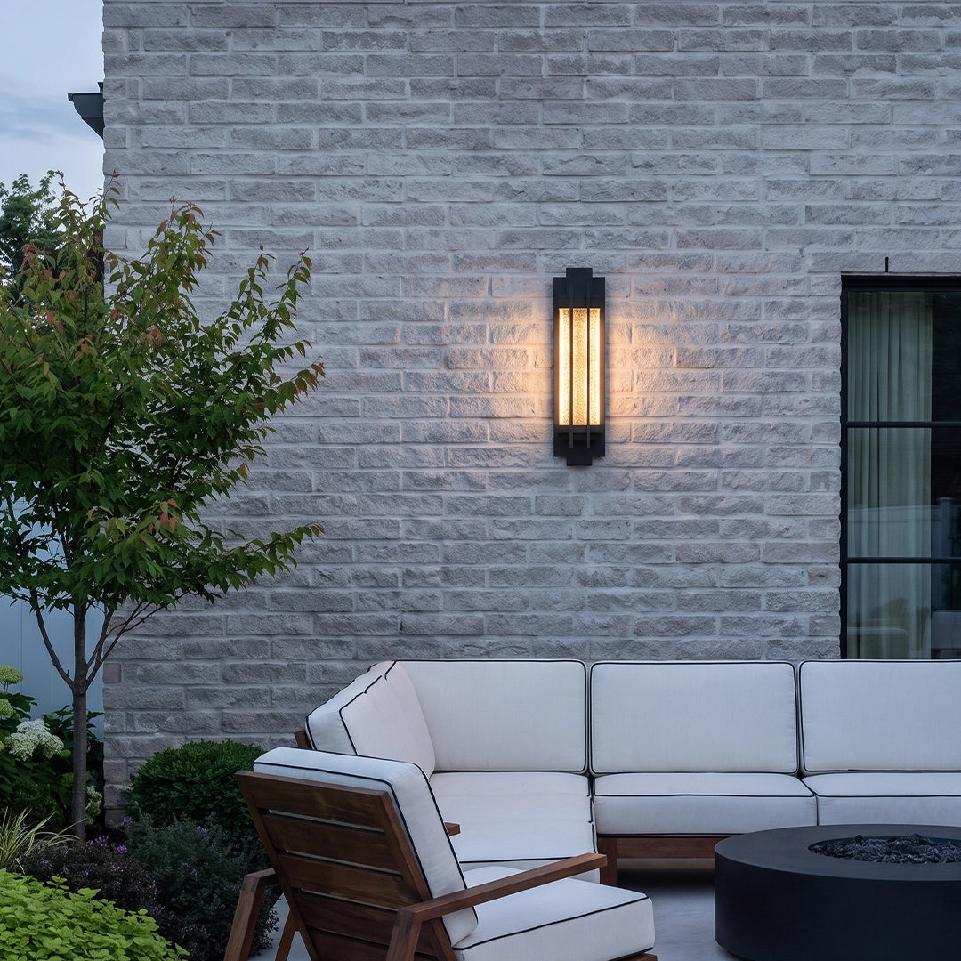 Black outside wall lights casting warm light over an outdoor lounge area against a white brick wall.