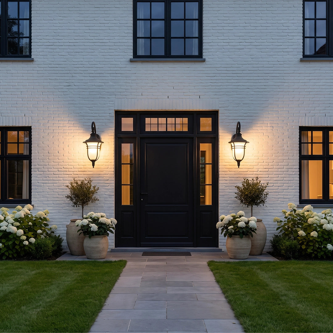 Black outside wall lights installed around a modern black entry door on a white brick home.