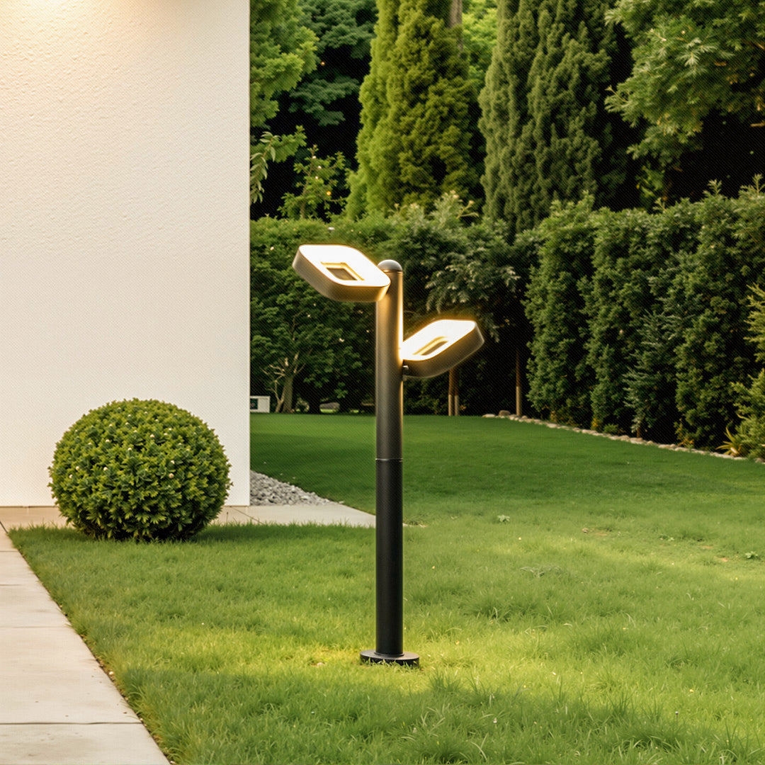 Modern black path light installed in a green garden lawn, illuminating the surrounding landscape.