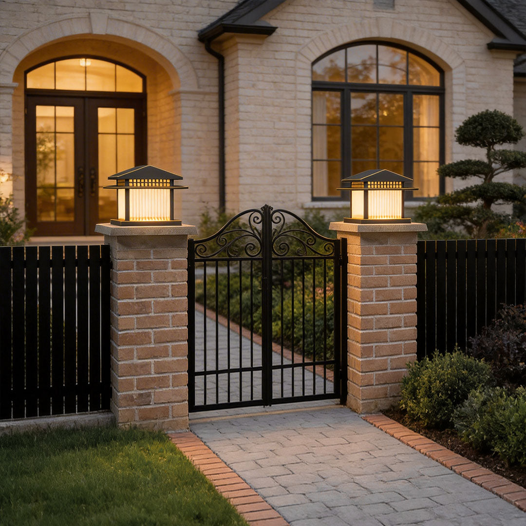 Classic black pillar lamp light mounted on a brick pillar beside a wrought iron gate.