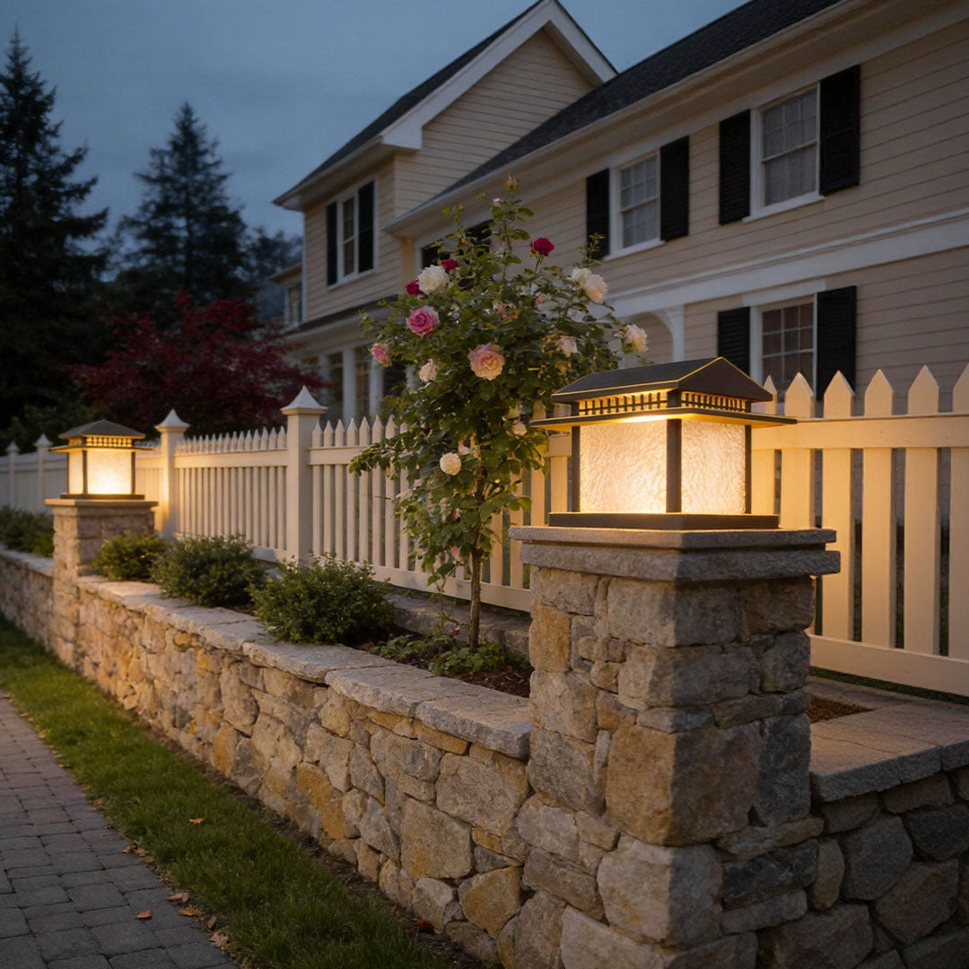 Elegant black pillar lamp light illuminating a stone wall along a garden pathway with lush greenery.
