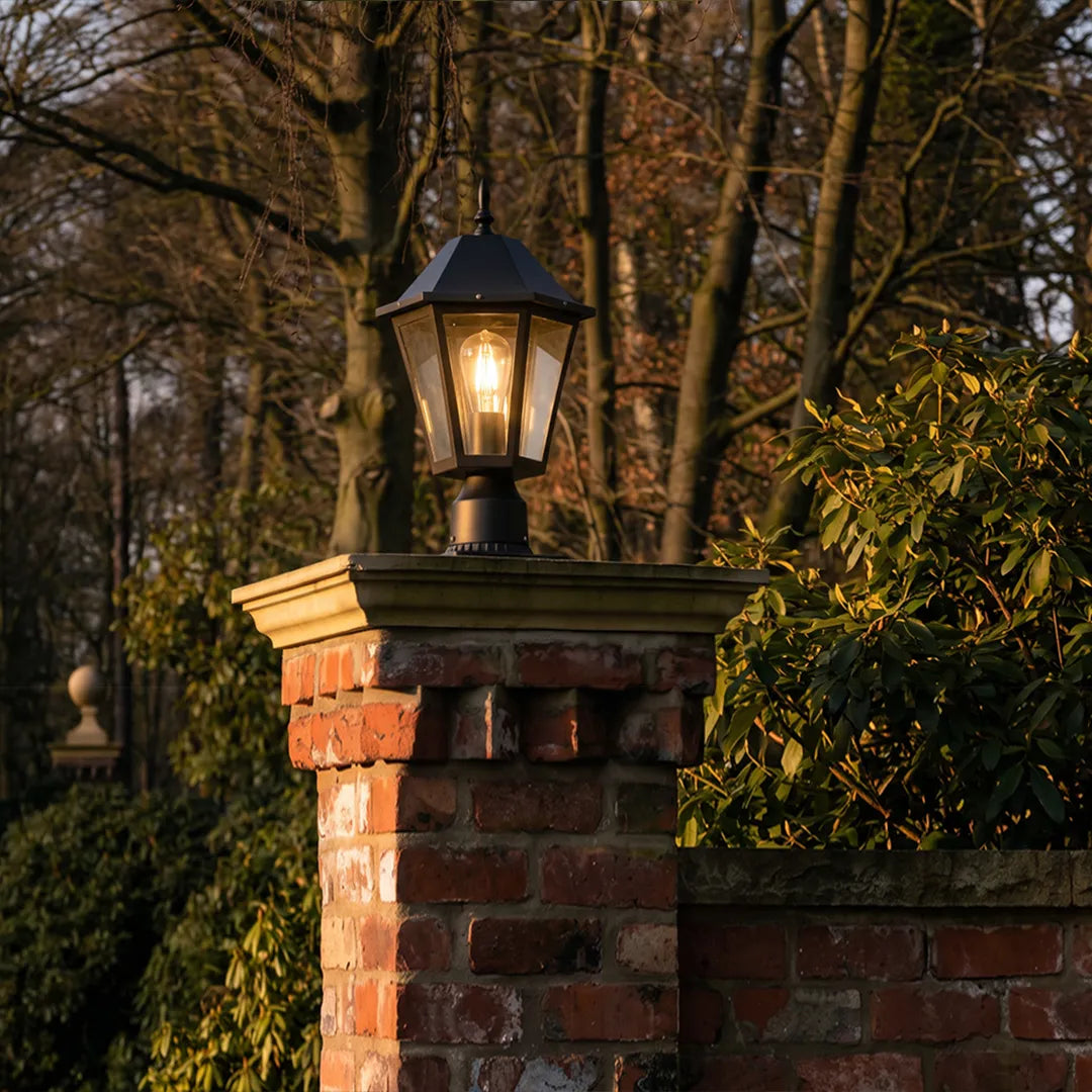 Black pillar light mounted on a brick pillar in a wooded outdoor setting, creating a timeless traditional accent.