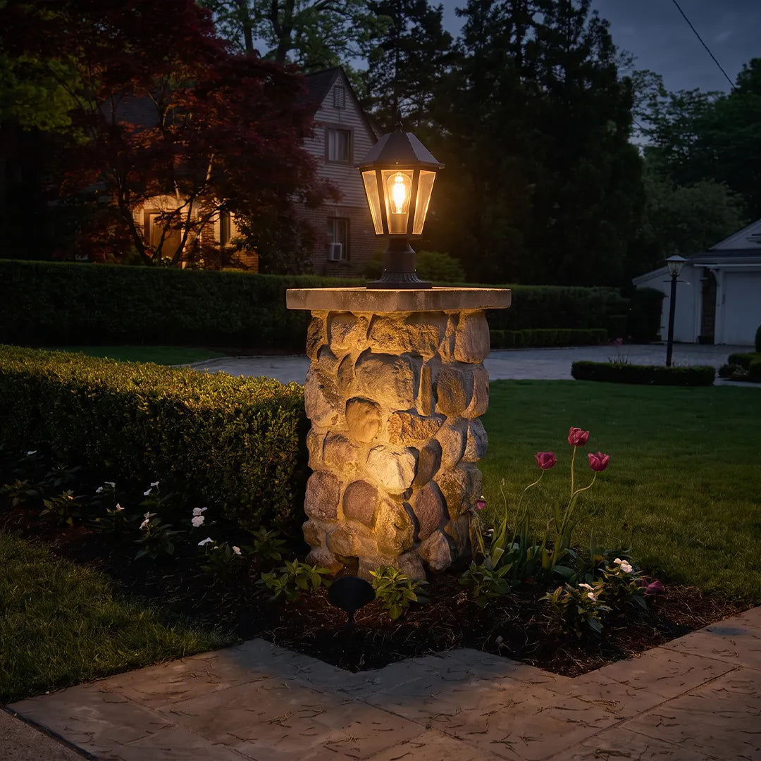 Black pillar light installed on a stone garden pillar at night, casting a warm glow across the landscape.