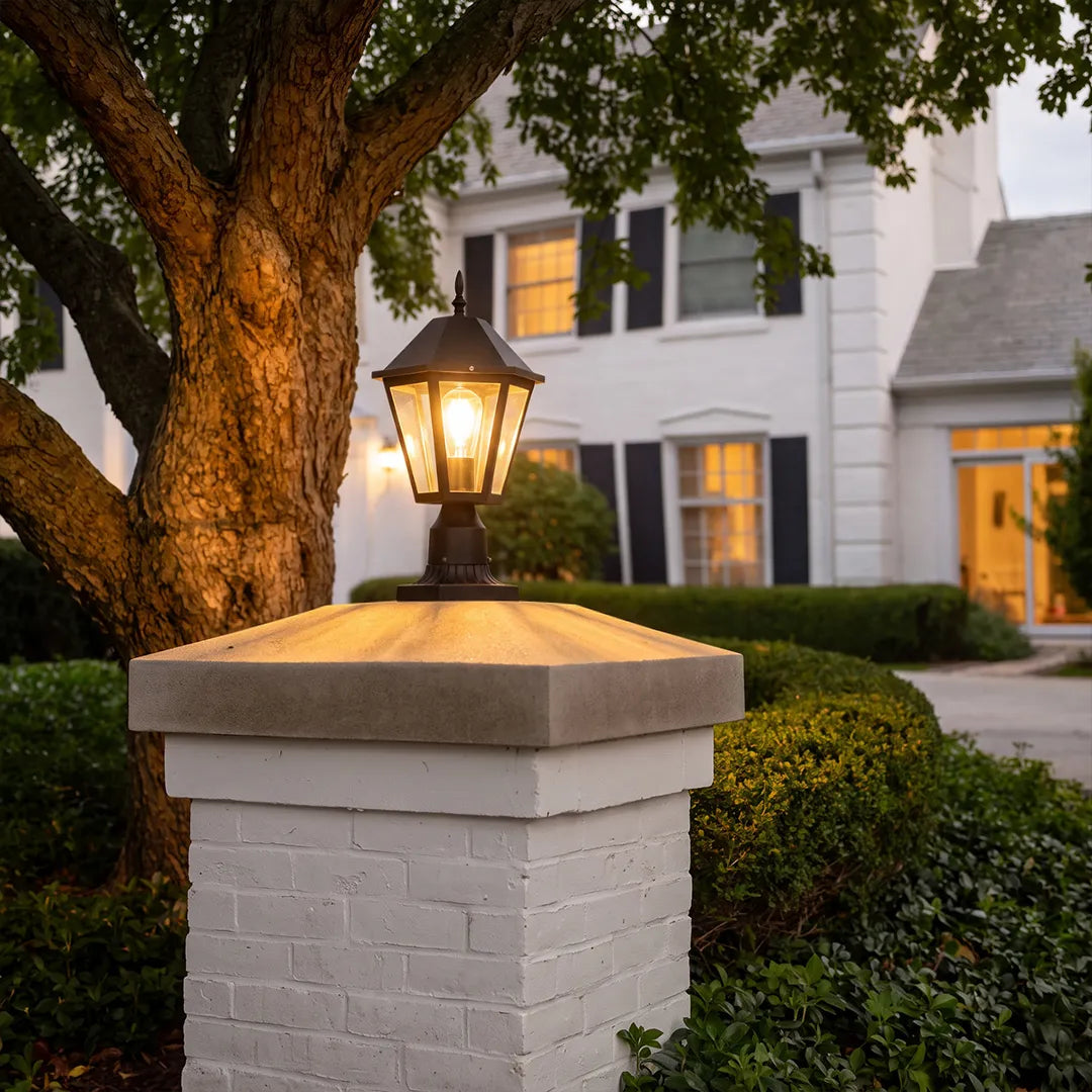 Black pillar light installed on a white brick fence post, bringing classic outdoor lighting to a landscaped entry.