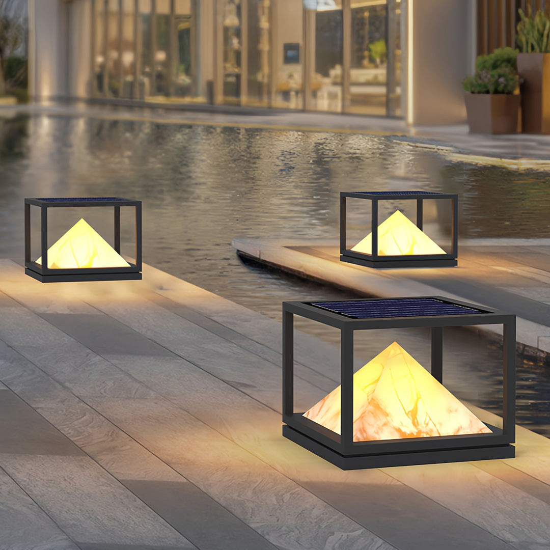Warm glowing pyramid outdoor lights placed on stone seating area in elegant light pillar design.