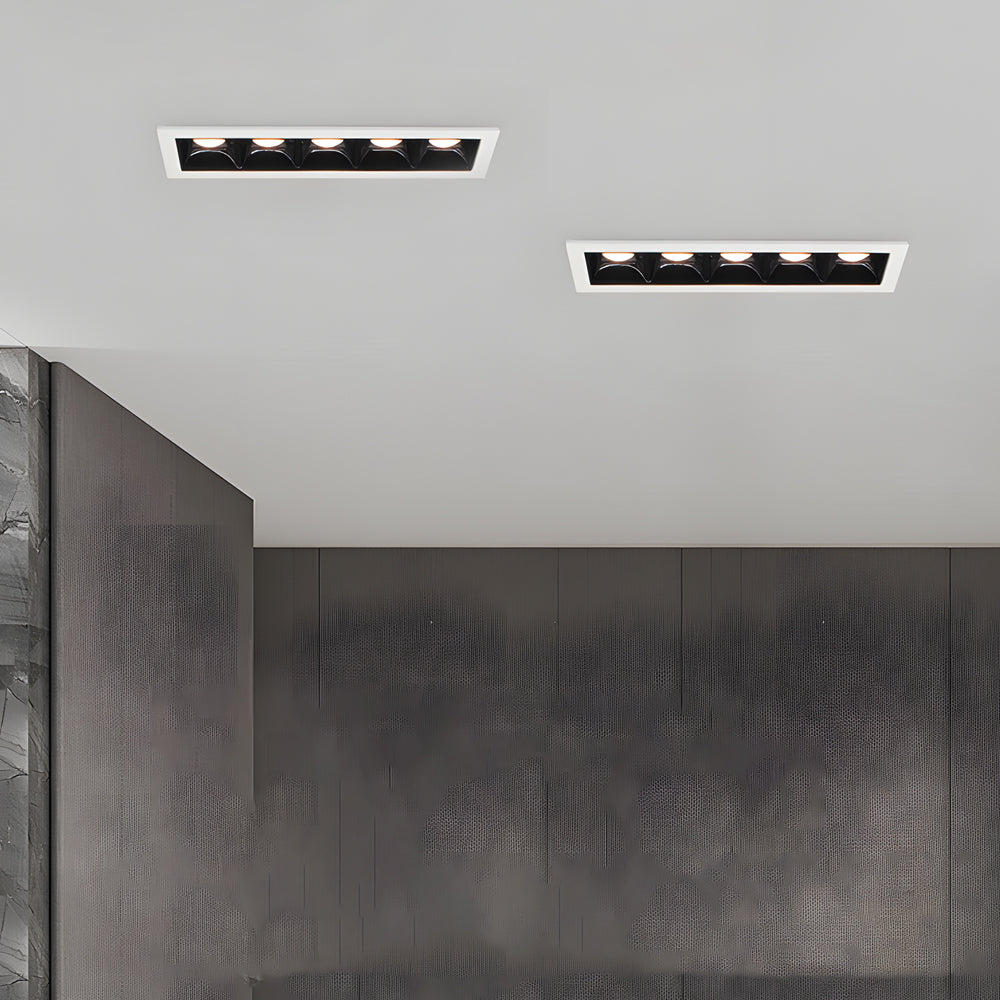 Black recessed ceiling spot lights creating focused illumination on concrete wall interior.