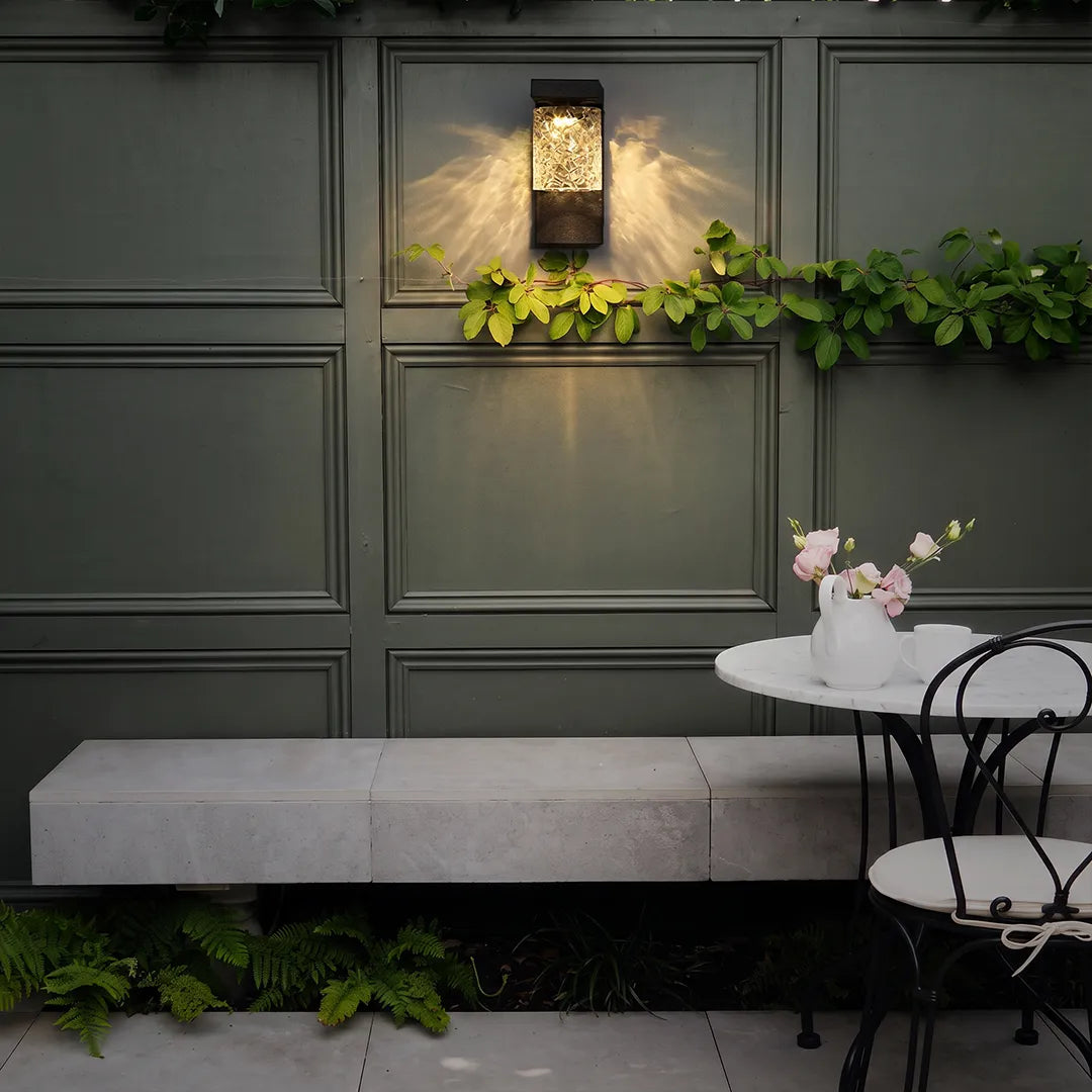 Black sconce wall light mounted on a dark garden wall above a built-in bench.