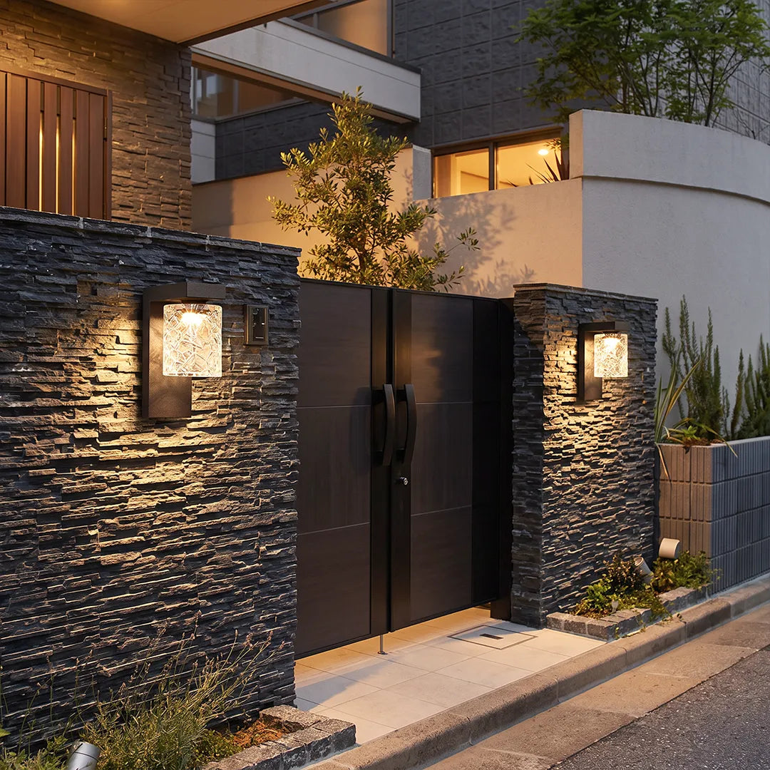 Black sconce wall light mounted on a stone garden wall beside a modern gate entrance.