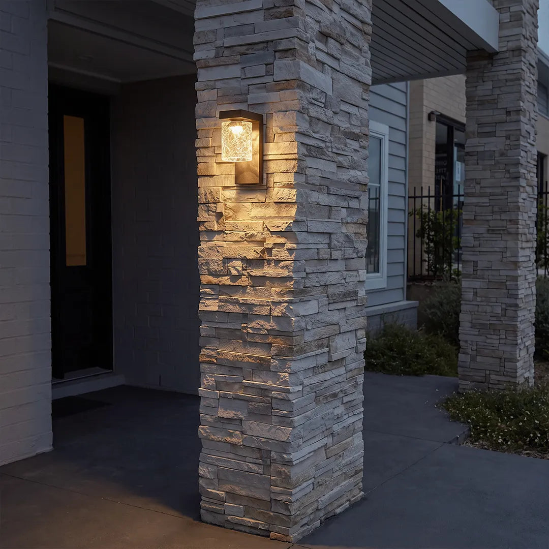 Black sconce wall light installed on a stone porch column outside a modern home.