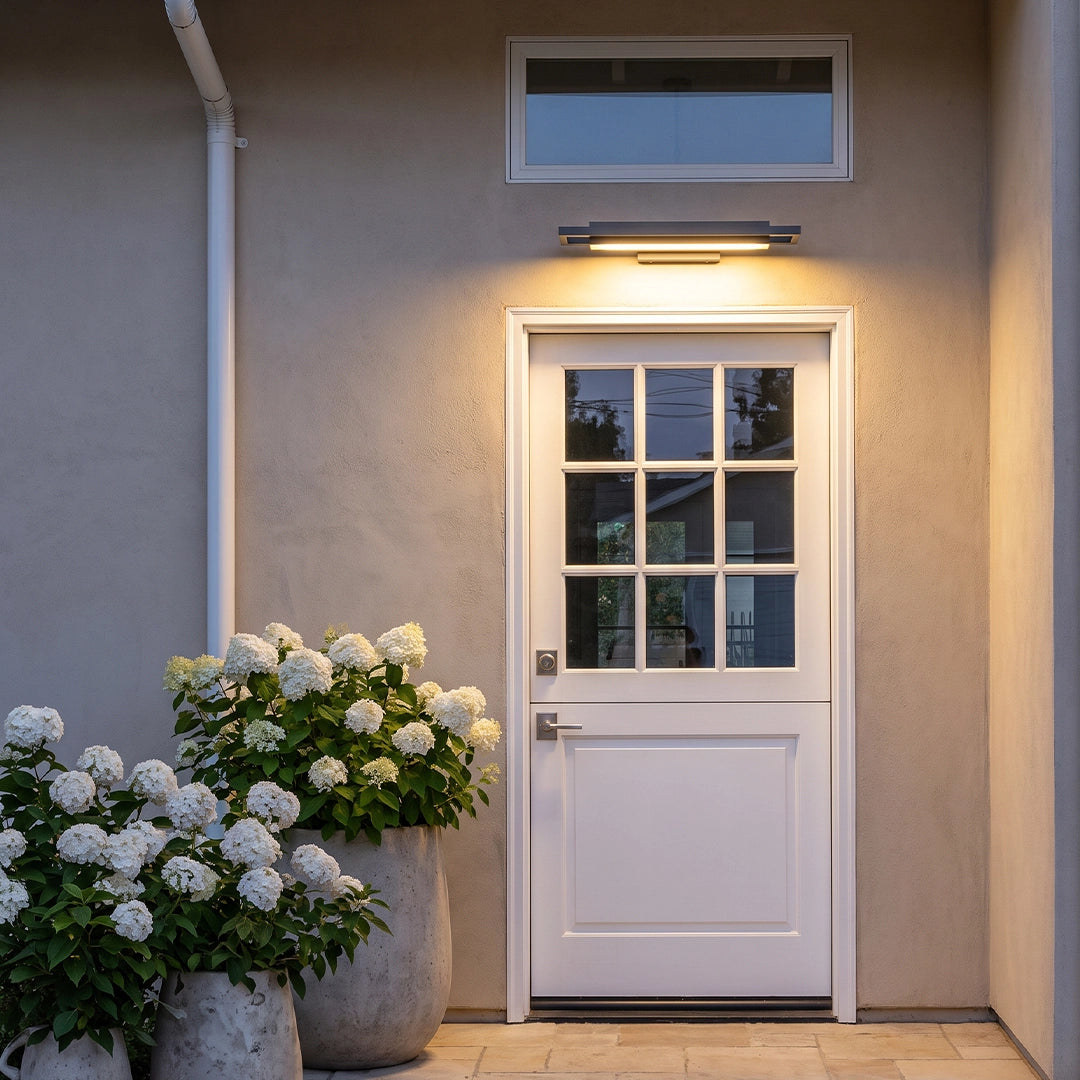 Black sconce wall lights casting warm light above a back door surrounded by white flowers.